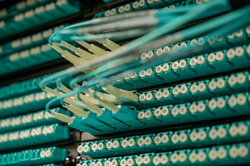 Painel de distribuição óptica com dezenas de conectores e cabos de fibra em tom verde-azulado