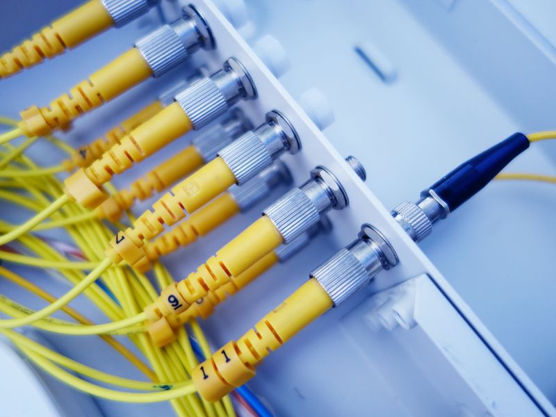 Conectores ópticos amarelos alinhados em equipamento de rede sobre fundo claro